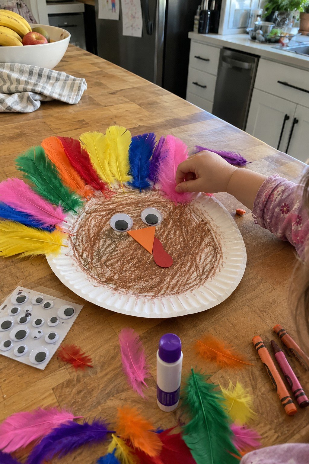 Paper plate turkey toddler craft with colorful feathers and googly eyes